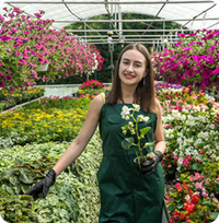 An image of an employee, smiling and holding up a plant
